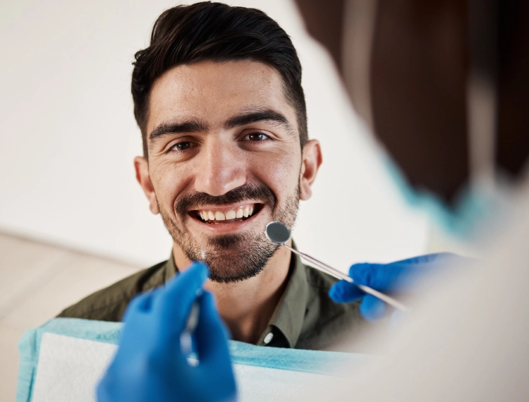 Smiling man receiving a dental checkup from a dentist wearing blue gloves and holding dental tools.